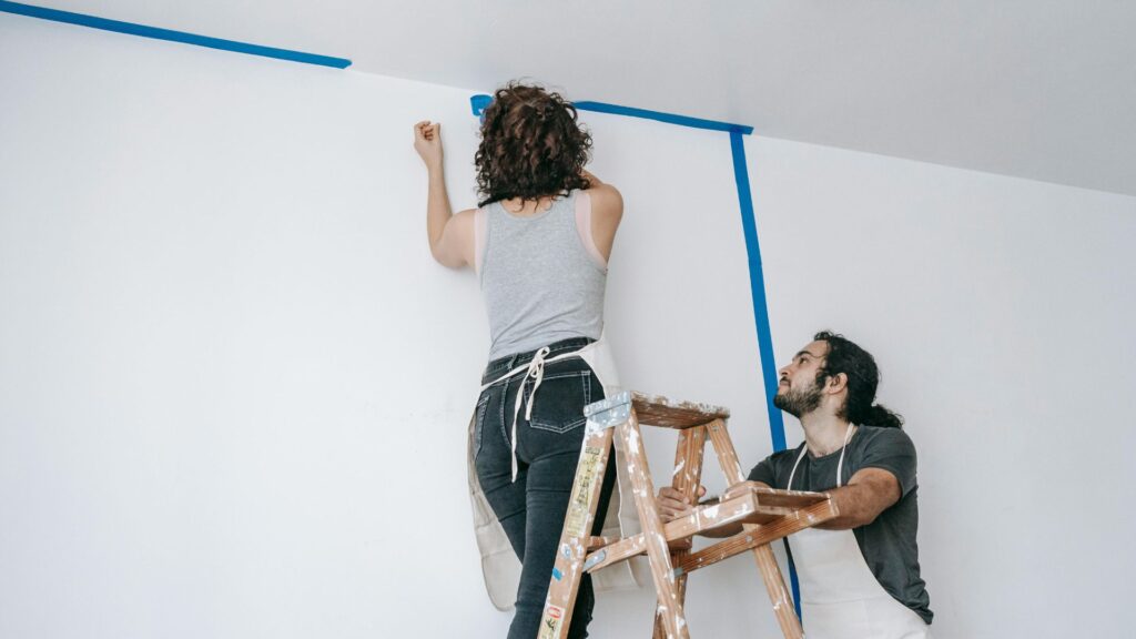Woman On A Stepladder Painting A Wall
